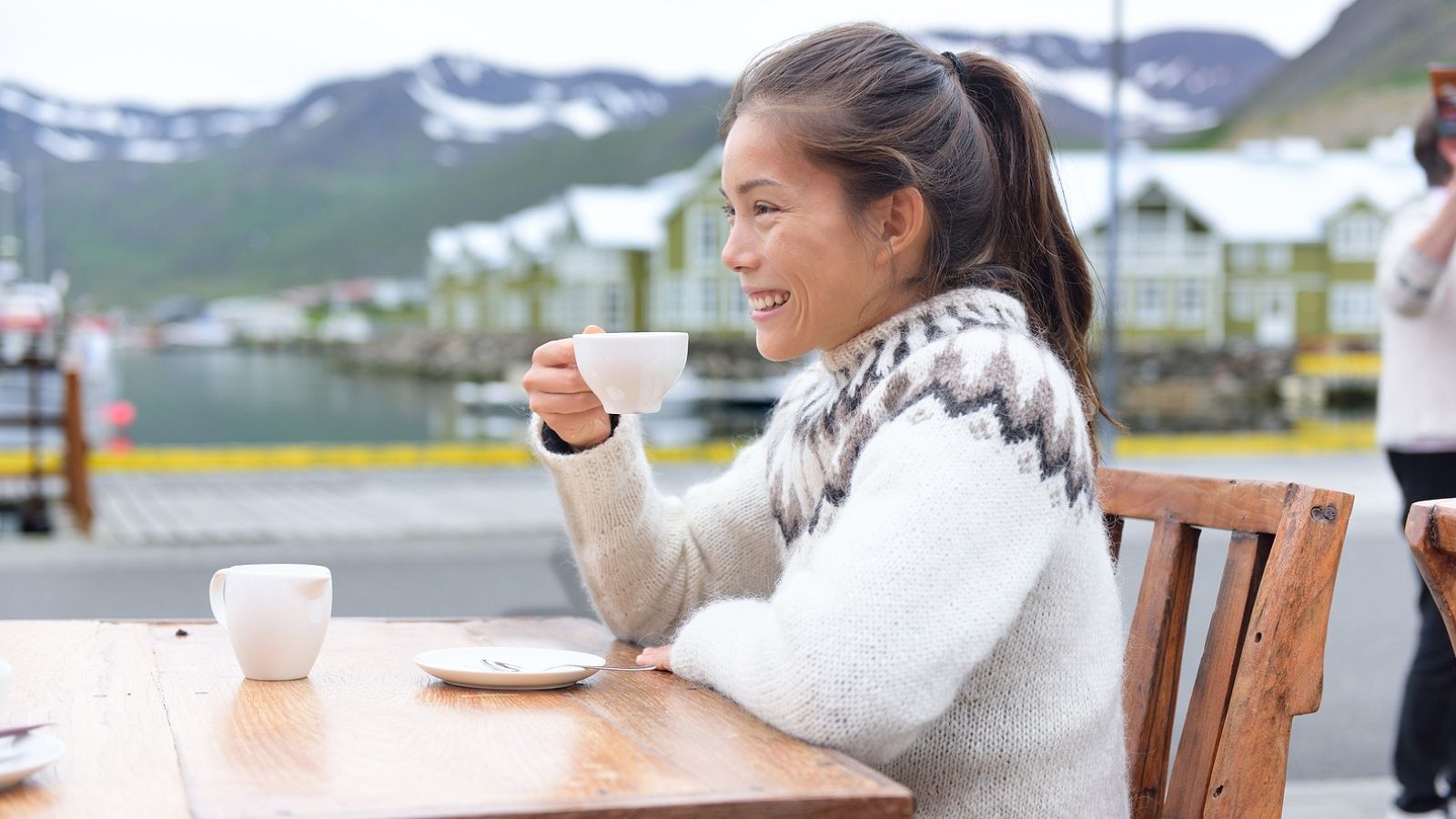 Woman wearing an Icelandic sweater enjoying a coffee at an outside table at a cafe.