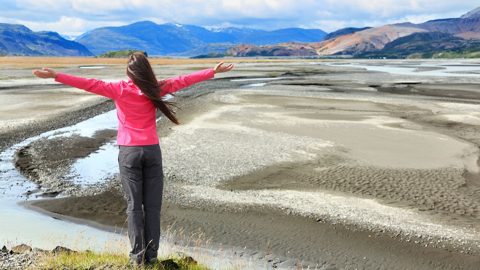 Woman standing with arms spread overlooking the Icelandic landscape.