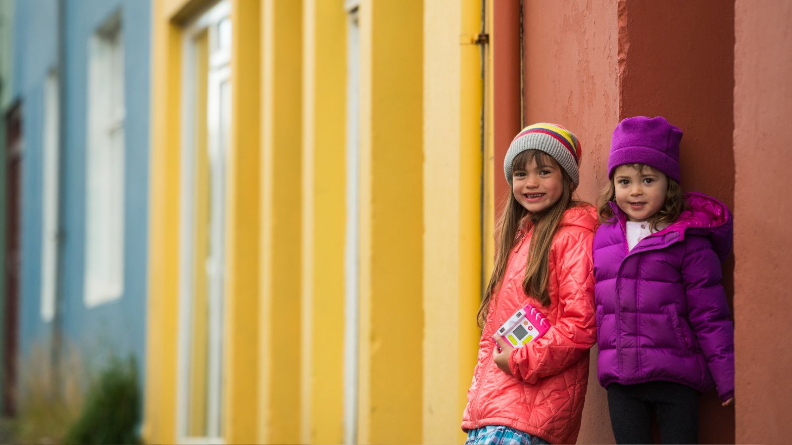 Two little girls standing next to colorful buildings in Reykjavík, Iceland. 