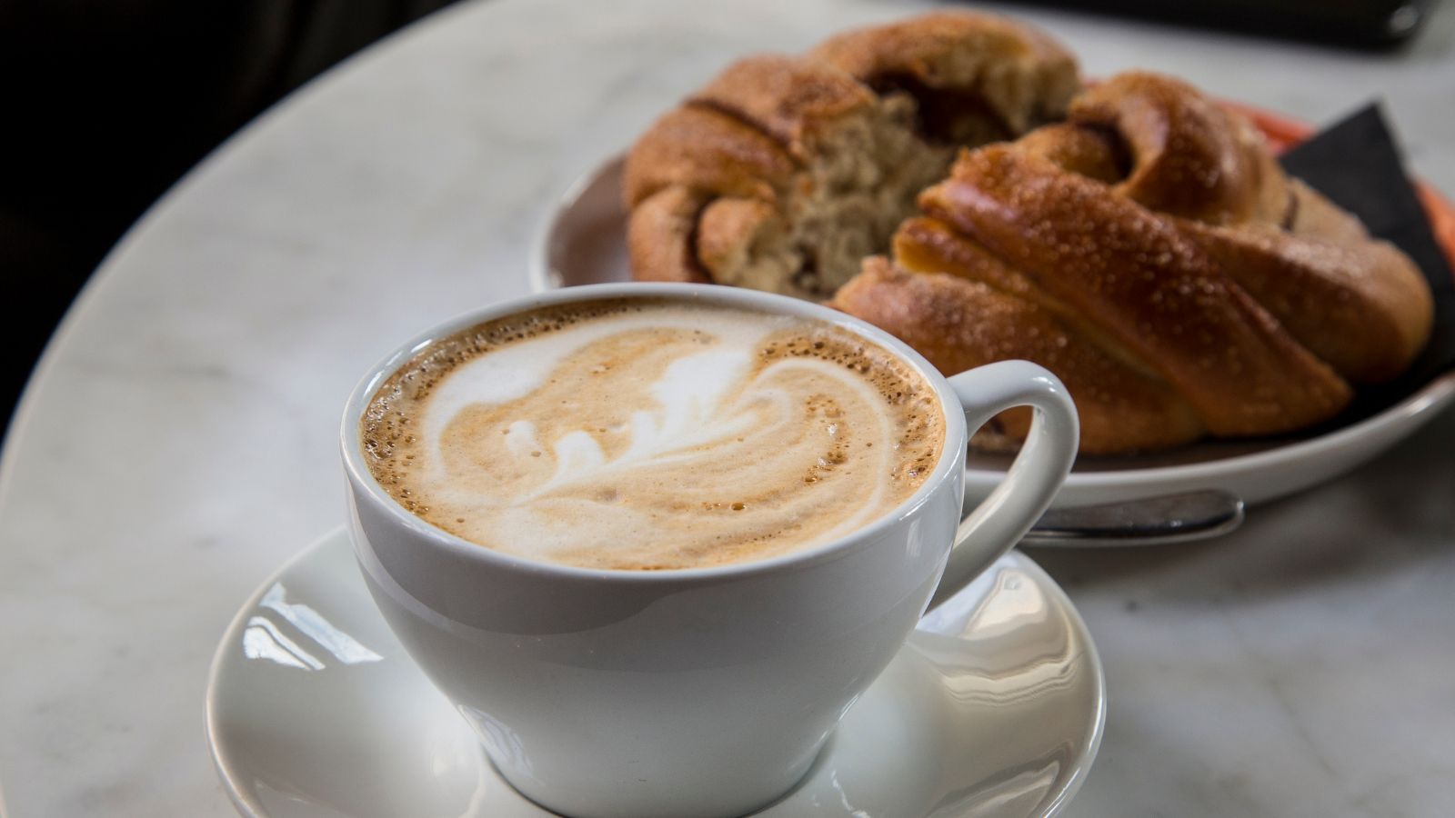 Close-up of a milky coffee and pastry on a table. 