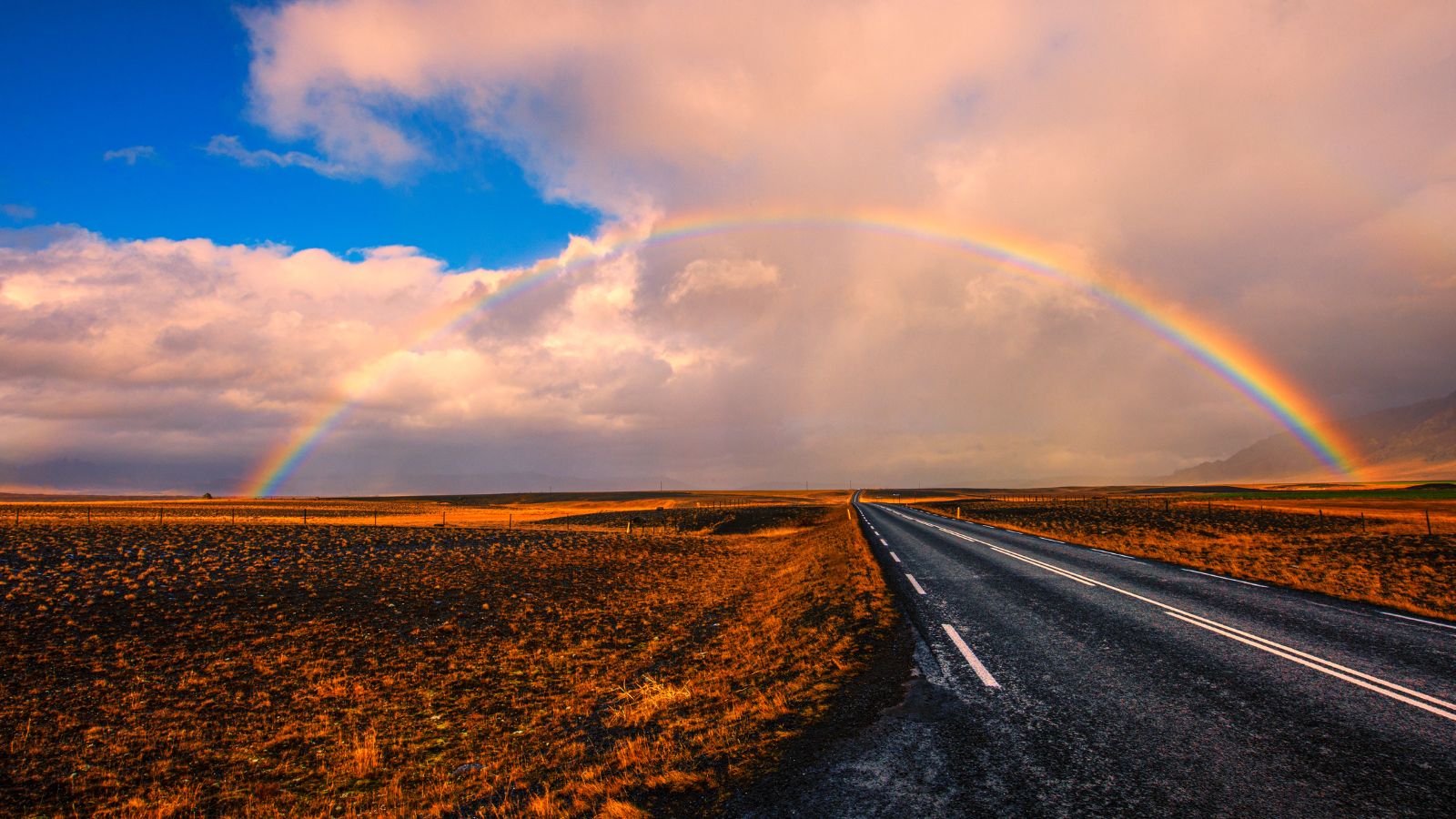 Rainbow in a dramatic sky over a road in Iceland.