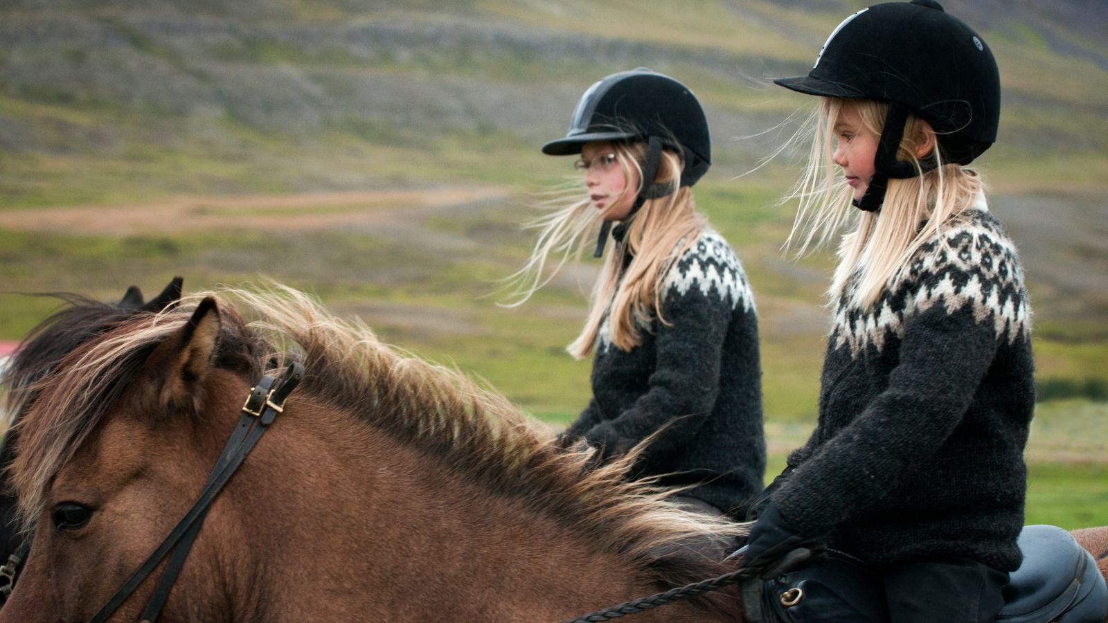 Two young girls riding Icelandic horses in Iceland.