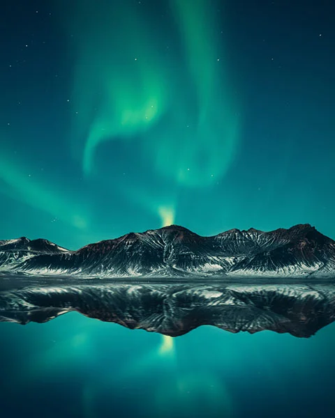 Aurora borealis over a mountain reflecting in a lake.